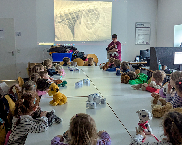 Tierärztin erklärt einer Kindergartengruppe in der Tierklinik Ismaning ein Röntgenbild, während die Kinder mit ihren Stofftieren zuhören.
